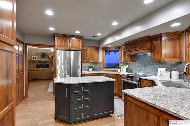 kitchen with appliances with stainless steel finishes, sink, light wood-type flooring, light stone counters, and decorative backsplash