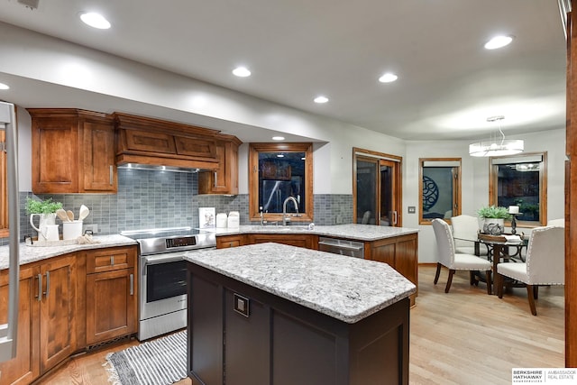 kitchen with light wood-type flooring, a center island, stainless steel appliances, sink, and light stone counters