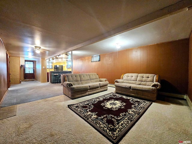 carpeted living room featuring ceiling fan, beamed ceiling, wood walls, and bar