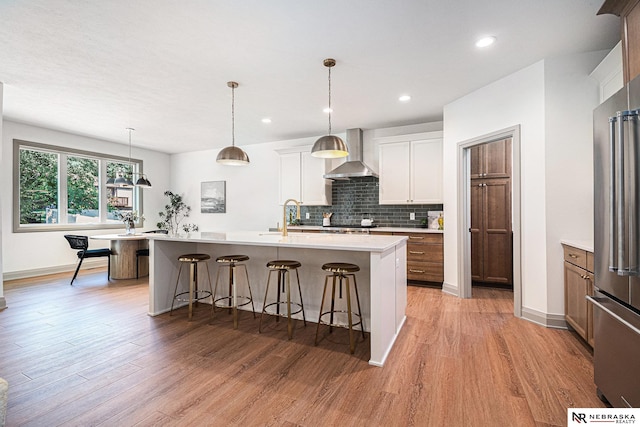 kitchen featuring wall chimney exhaust hood, light hardwood / wood-style floors, high end refrigerator, a center island with sink, and white cabinets