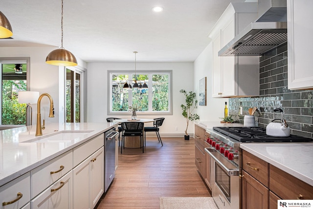 kitchen with stainless steel appliances, white cabinets, wall chimney exhaust hood, and sink