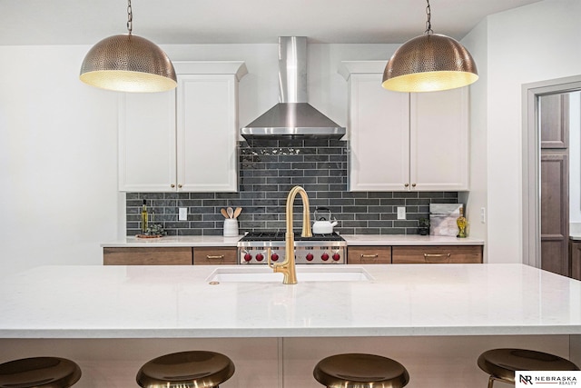 kitchen featuring wall chimney range hood, hanging light fixtures, and white cabinetry