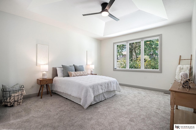 carpeted bedroom with ceiling fan and a raised ceiling