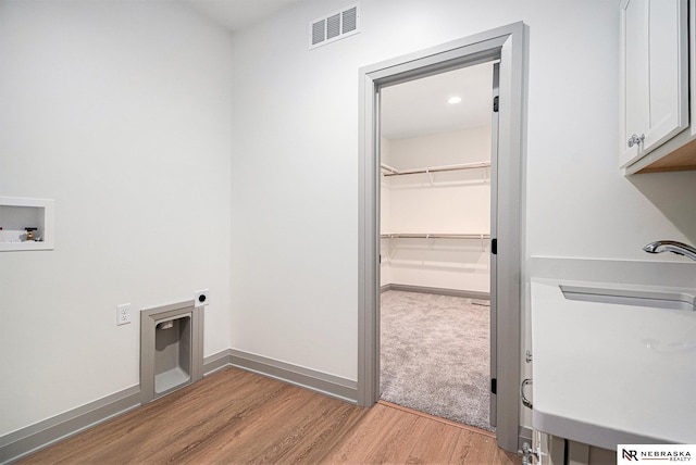 clothes washing area with electric dryer hookup, light wood-type flooring, washer hookup, and cabinets