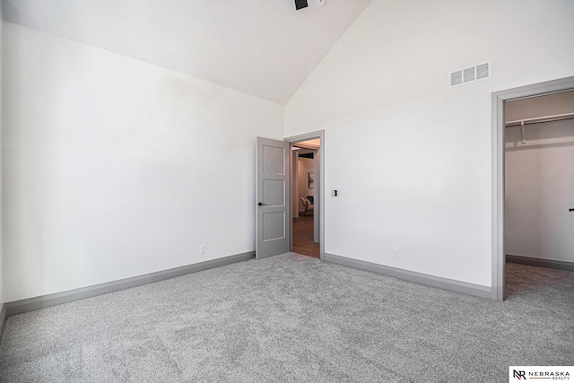 unfurnished bedroom with a closet, high vaulted ceiling, a walk in closet, and carpet