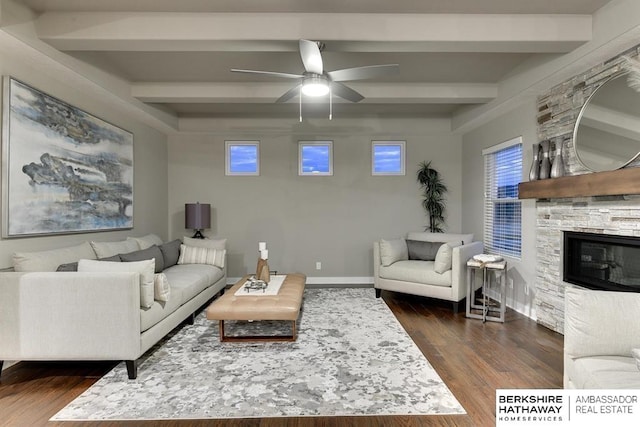 living room featuring beamed ceiling, ceiling fan, dark wood-type flooring, and a stone fireplace