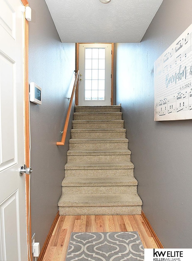 stairs with a textured ceiling and wood-type flooring