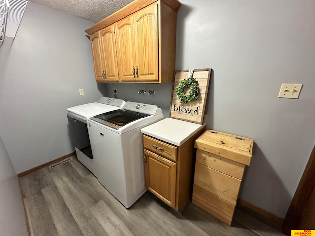 laundry room featuring a textured ceiling, wood-type flooring, cabinets, and separate washer and dryer