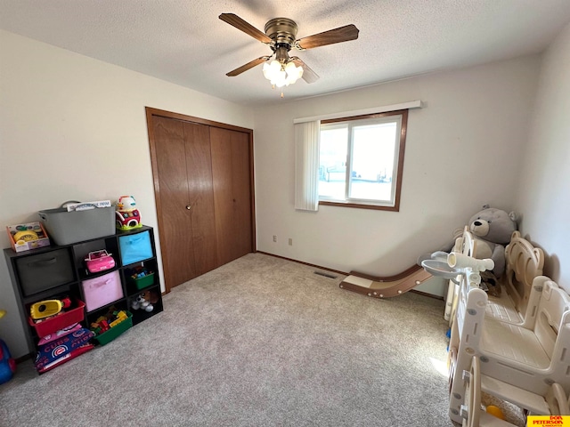 rec room with a textured ceiling, light colored carpet, and ceiling fan