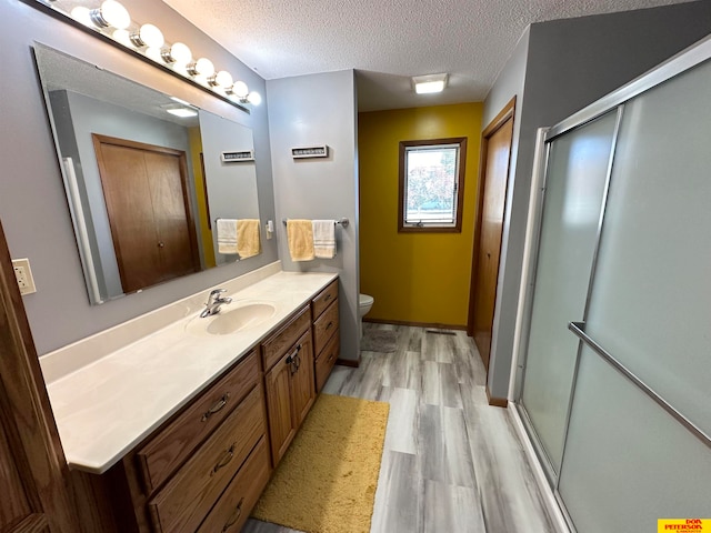 bathroom featuring a textured ceiling, hardwood / wood-style flooring, toilet, vanity, and an enclosed shower