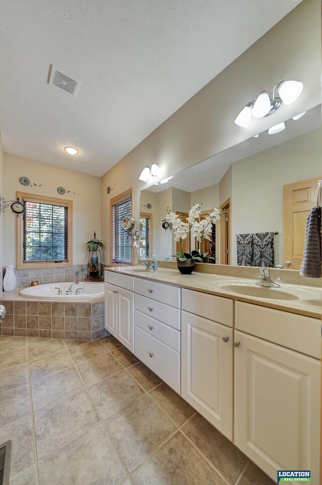 bathroom with vanity, a relaxing tiled tub, a textured ceiling, and tile patterned floors