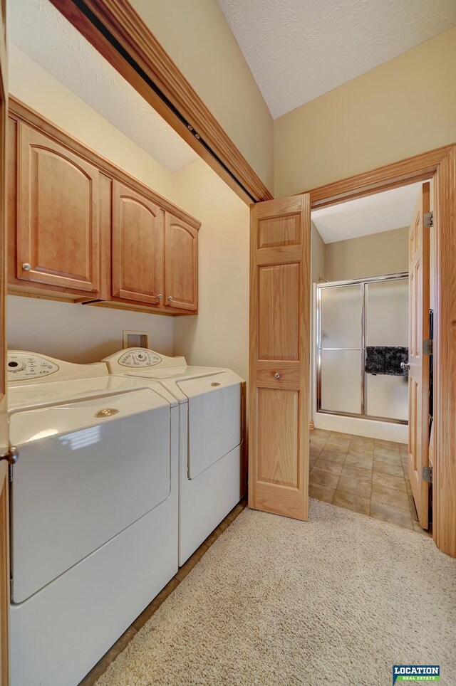 laundry area with a textured ceiling, cabinets, washer and clothes dryer, and light colored carpet