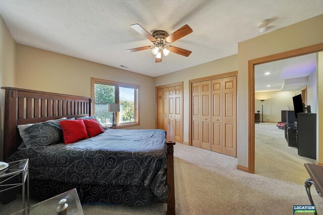 carpeted bedroom featuring a textured ceiling, multiple closets, and ceiling fan