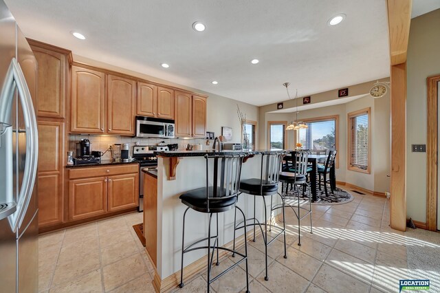 kitchen with a kitchen island with sink, a breakfast bar area, backsplash, decorative light fixtures, and appliances with stainless steel finishes