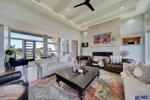 living room with a high ceiling, beam ceiling, wood-type flooring, a fireplace, and ceiling fan