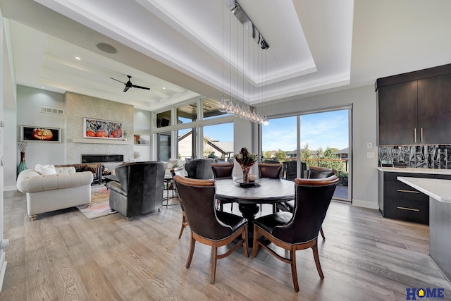 dining area featuring light hardwood / wood-style flooring, a large fireplace, a tray ceiling, and ceiling fan