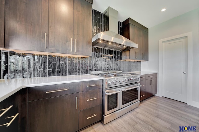 kitchen featuring backsplash, dark brown cabinets, wall chimney exhaust hood, light hardwood / wood-style flooring, and double oven range