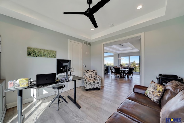 home office with a tray ceiling, light wood-type flooring, and ceiling fan