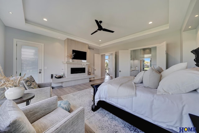 bedroom featuring ceiling fan, a fireplace, a tray ceiling, and light hardwood / wood-style floors