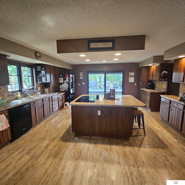 kitchen with a kitchen island, light hardwood / wood-style flooring, a wealth of natural light, sink, and black appliances