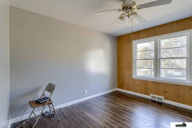 unfurnished room featuring ceiling fan, dark hardwood / wood-style floors, and wood walls