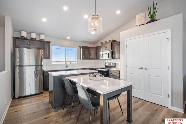 kitchen featuring stainless steel appliances, vaulted ceiling, a kitchen island, and hanging light fixtures