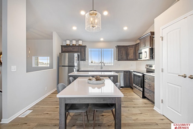 kitchen with appliances with stainless steel finishes, light hardwood / wood-style flooring, a healthy amount of sunlight, and hanging light fixtures