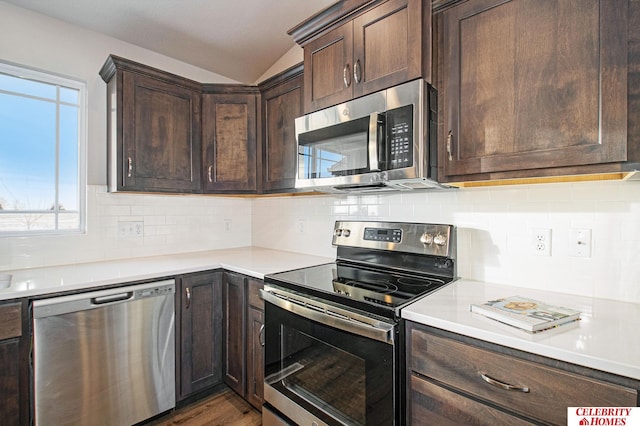 kitchen with decorative backsplash, wood-type flooring, vaulted ceiling, dark brown cabinetry, and appliances with stainless steel finishes