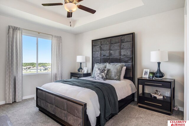 carpeted bedroom with a raised ceiling and ceiling fan