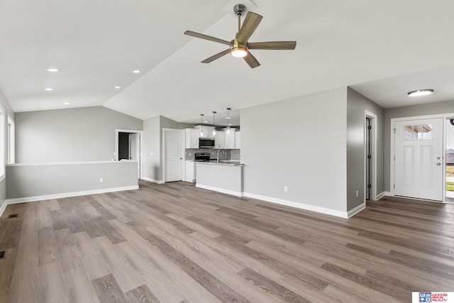 unfurnished living room featuring sink, ceiling fan, vaulted ceiling, and light wood-type flooring