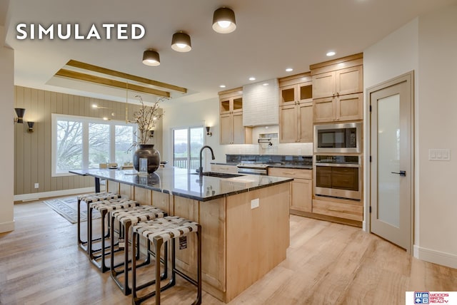 kitchen with a spacious island, light hardwood / wood-style flooring, stainless steel appliances, dark stone counters, and sink