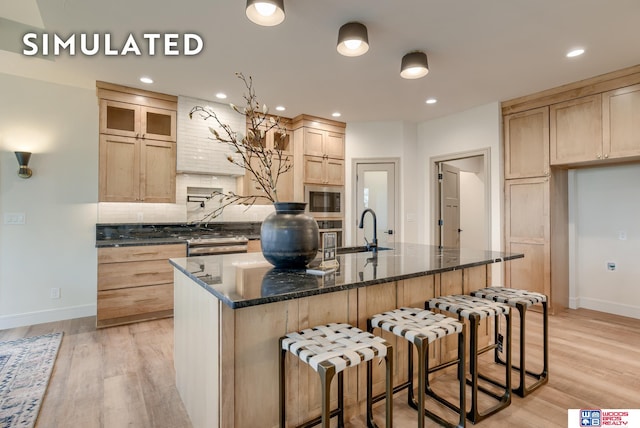 kitchen featuring stainless steel microwave, light hardwood / wood-style flooring, sink, and a kitchen island with sink