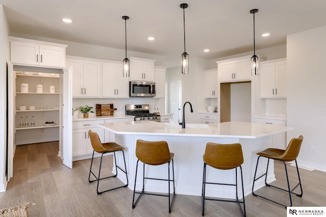 kitchen featuring white cabinetry, stainless steel appliances, and an island with sink