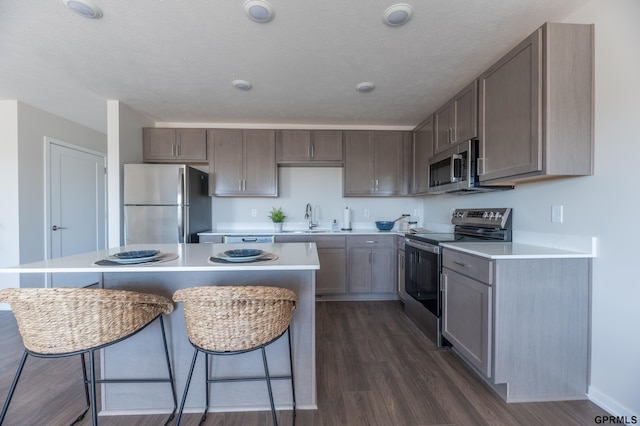 kitchen with dark wood-style floors, a kitchen breakfast bar, a sink, and appliances with stainless steel finishes