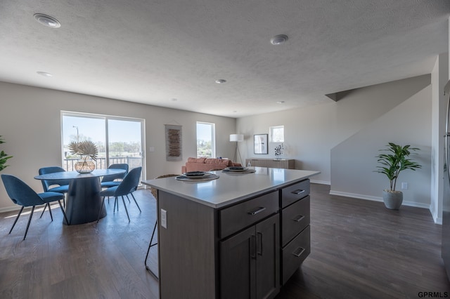 kitchen with a textured ceiling, baseboards, dark wood finished floors, and a center island