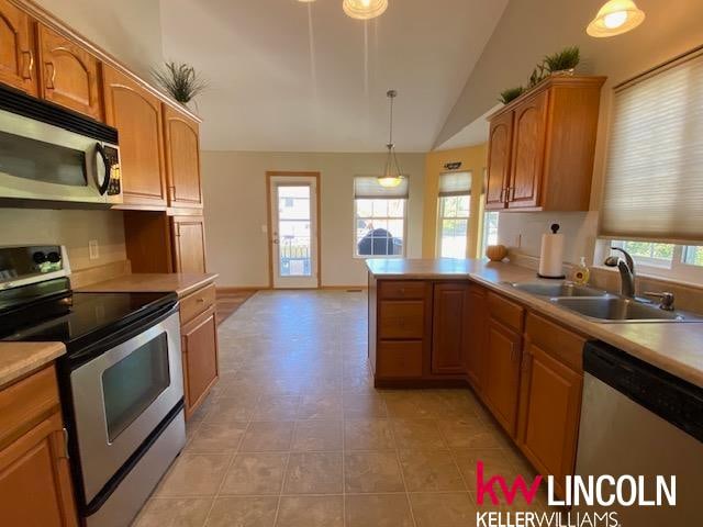 kitchen featuring sink, kitchen peninsula, stainless steel appliances, lofted ceiling, and decorative light fixtures