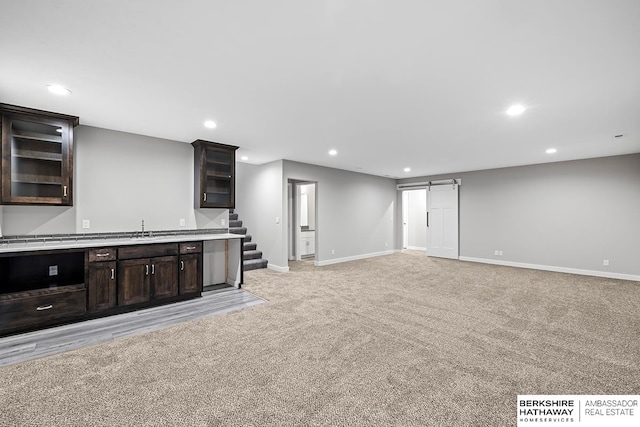 unfurnished living room featuring light colored carpet, wet bar, and a barn door