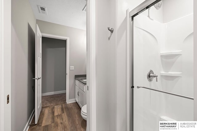 bathroom with a textured ceiling, hardwood / wood-style floors, toilet, walk in shower, and vanity