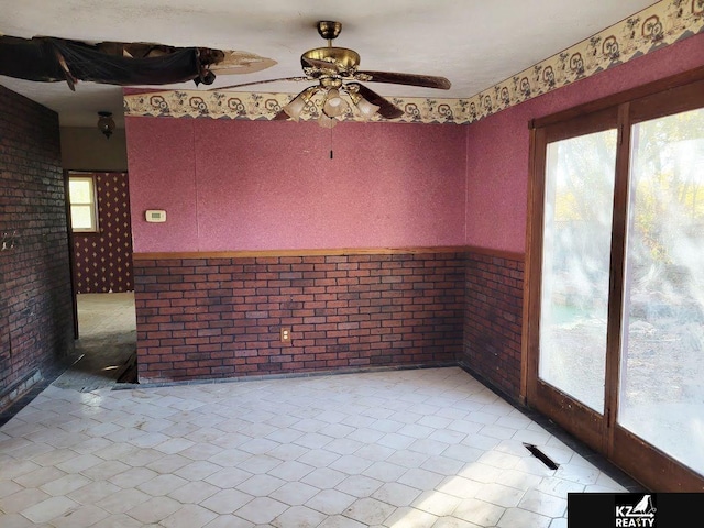 empty room featuring brick wall, a healthy amount of sunlight, and ceiling fan