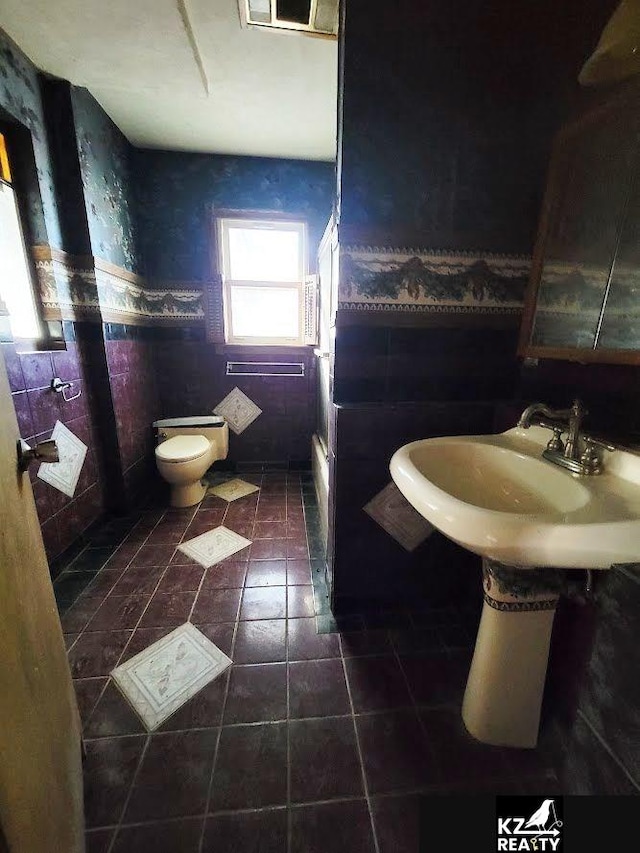 bathroom featuring toilet, tile patterned floors, and tile walls