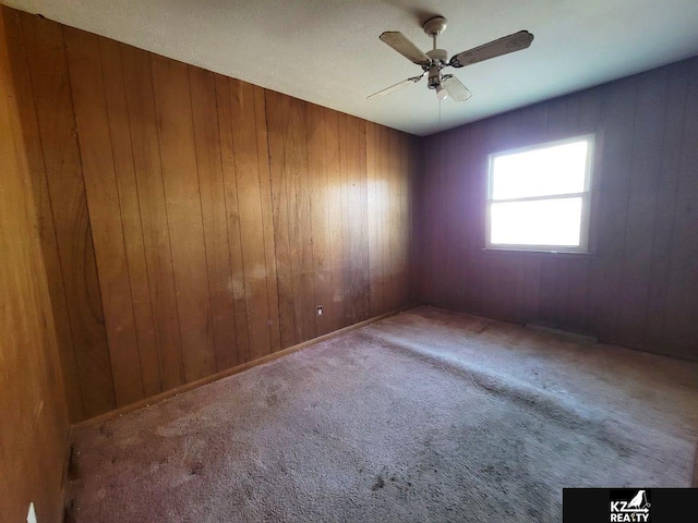 unfurnished room with ceiling fan, carpet flooring, and wooden walls