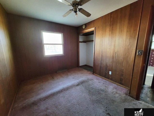 unfurnished bedroom featuring wood walls, carpet floors, a closet, and ceiling fan