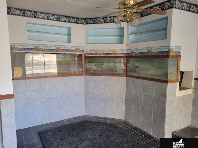 interior space featuring ceiling fan and tile walls