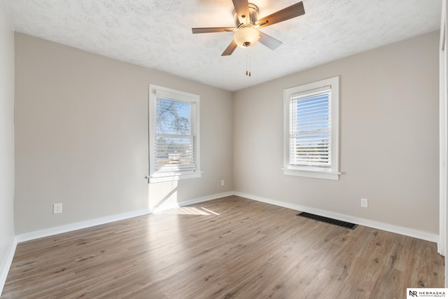 empty room featuring a textured ceiling, hardwood / wood-style flooring, a healthy amount of sunlight, and ceiling fan