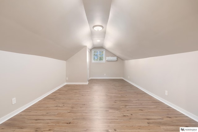 bonus room with lofted ceiling, a wall mounted AC, and light hardwood / wood-style floors