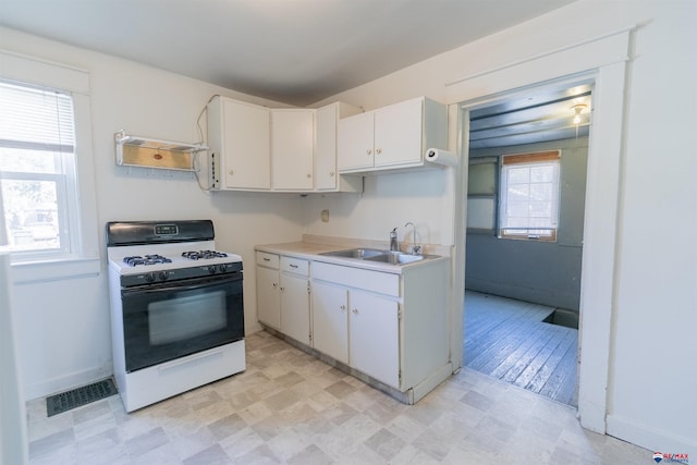 kitchen featuring white range with gas cooktop, white cabinets, and a healthy amount of sunlight