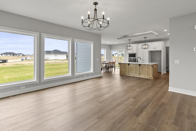 kitchen featuring visible vents, an inviting chandelier, light countertops, a kitchen island with sink, and wood finished floors