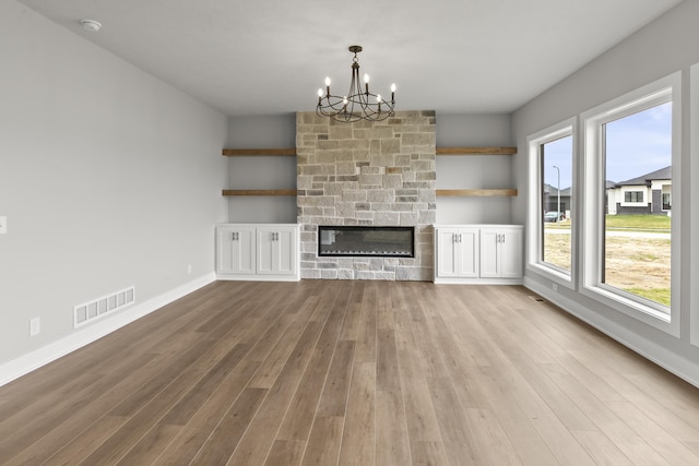 unfurnished living room featuring a notable chandelier, baseboards, a fireplace, visible vents, and wood finished floors