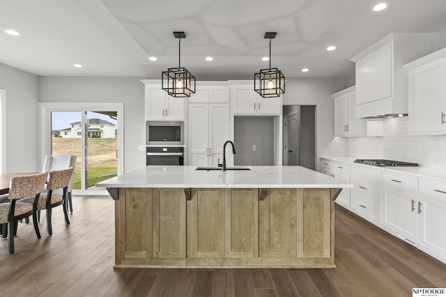 kitchen featuring dark wood-type flooring, tasteful backsplash, appliances with stainless steel finishes, a kitchen island with sink, and a sink