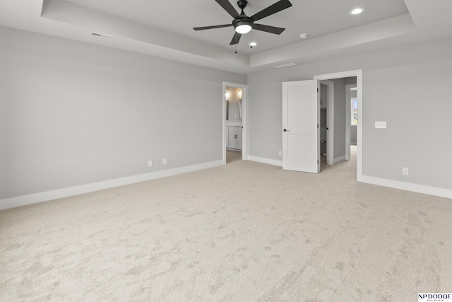 unfurnished bedroom with light carpet, visible vents, a tray ceiling, and baseboards